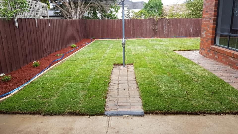 Same backyard after: fresh green turf laid with neat red mulch garden borders