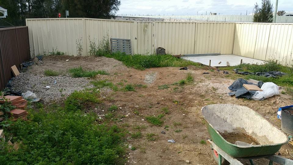 Backyard before work with weeds, rubble and a wheelbarrow of debris